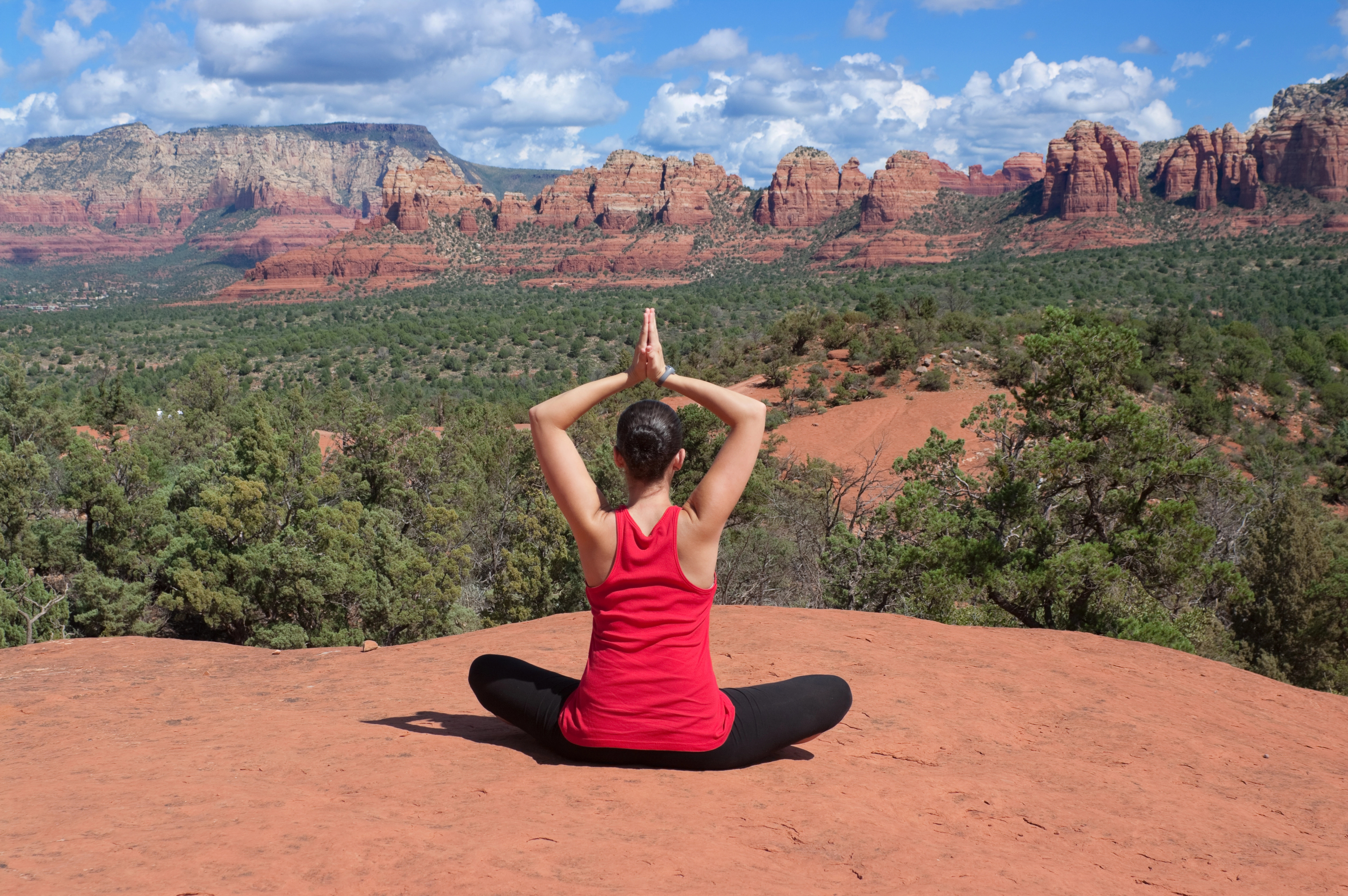 Woman meditating in yoga pose on red rock in Sedona, Arizona.