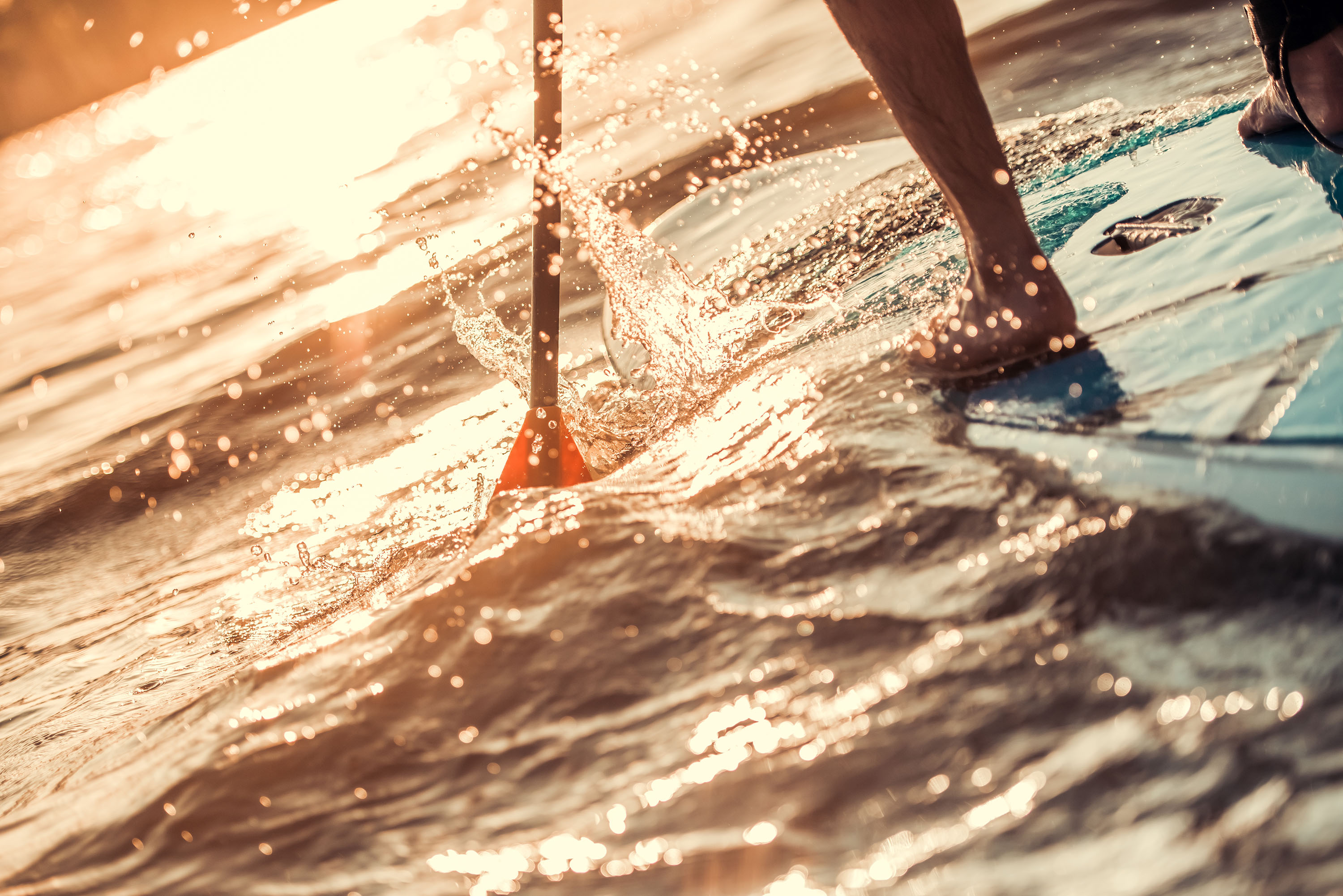 feet of person paddle boarding at sunset with paddle splashing in the water