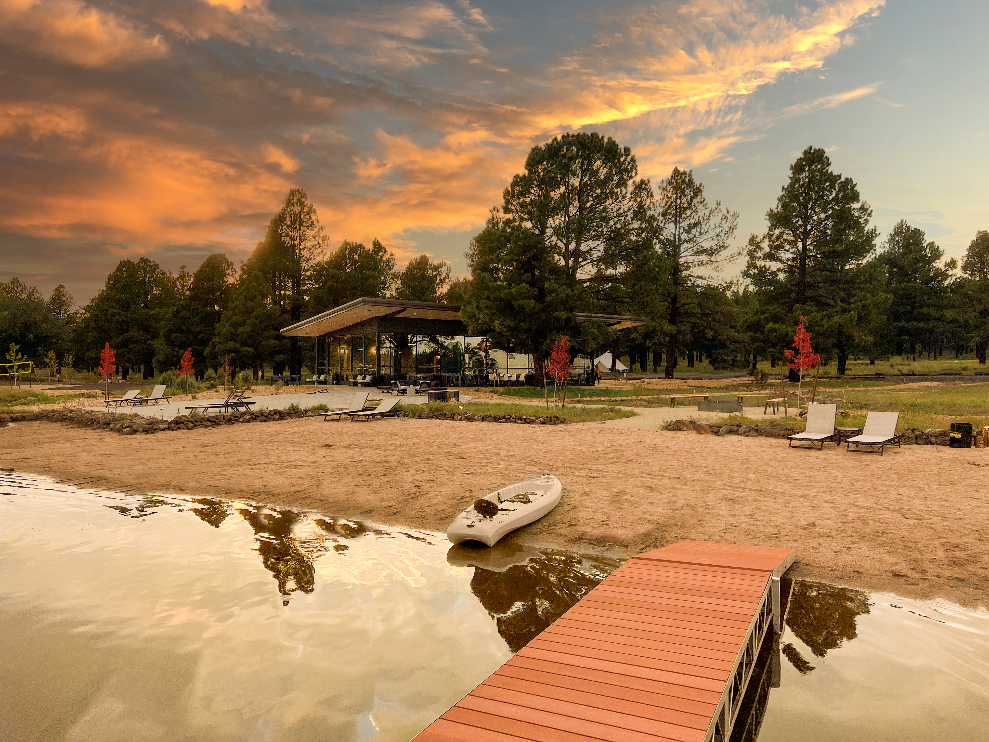 Calm water and a beach with kayak, dock and lounge chairs at sunset.