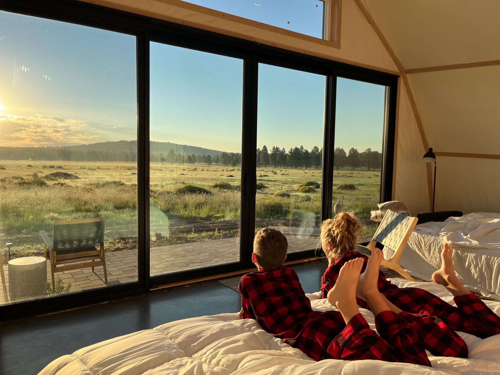 Boy and girl in matching pajamas watching sunrise over meadow through sliding glass doors
